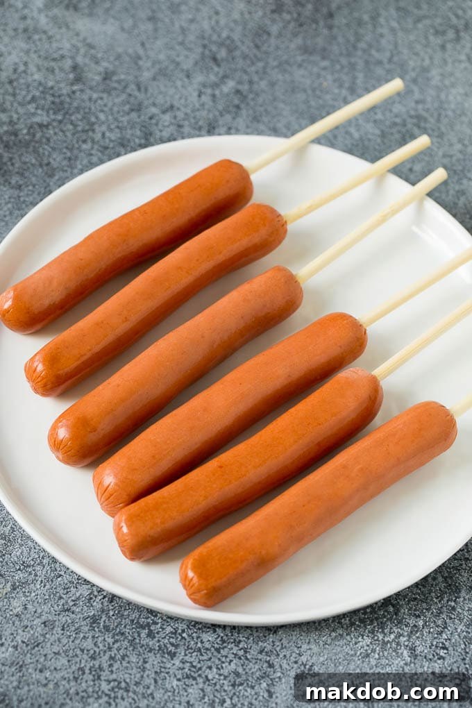 Homemade corn dogs are so easy to make and are even better than what you'd get at the fair! Hot dogs on sticks prepared for battering and frying.
