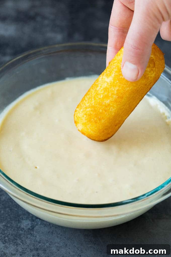 Fried Twinkies are a remake of the carnival classic that are fun and easy to make at home. A Twinkie being dipped into a bowl of batter.