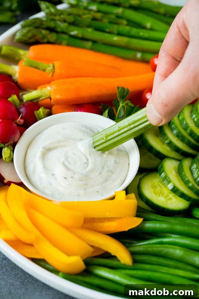 Enjoying a Fresh Veggie Tray: Dipping Celery in Ranch Sauce A hand gracefully dipping a crisp celery stick into a creamy, white ranch sauce, emphasizing the enjoyable act of snacking on a veggie tray.