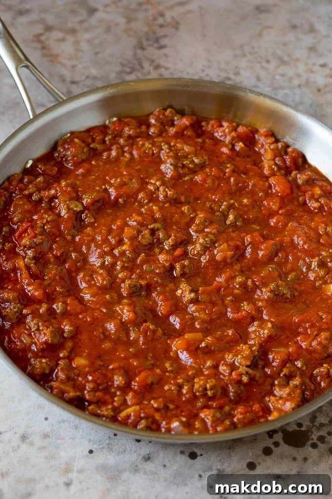 Rich meat sauce simmering in a skillet, with ground beef, onions, and garlic visible.