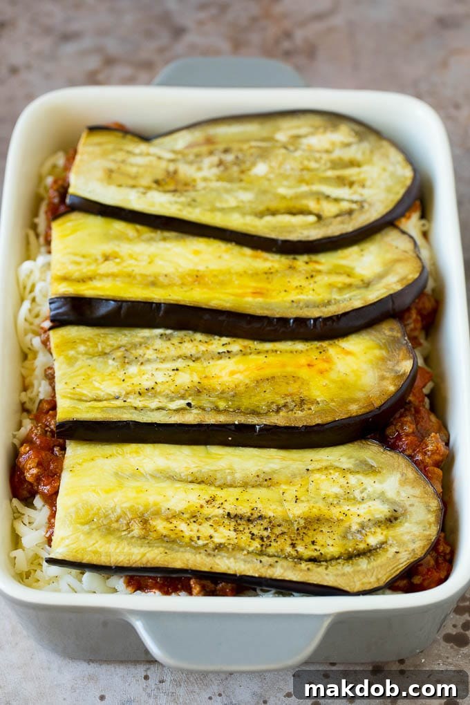 Close-up of layers of eggplant, meat sauce, and three types of cheese meticulously arranged in a baking dish, ready for baking.