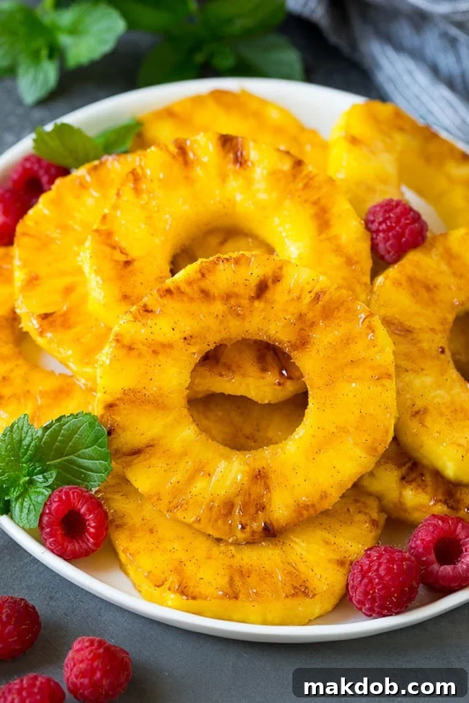 A plate of grilled pineapple slices garnished with raspberries and mint, showcasing the beautiful caramelization.