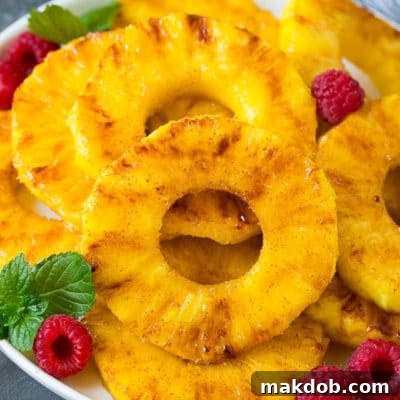 A plate of grilled pineapple slices garnished with raspberries and mint.