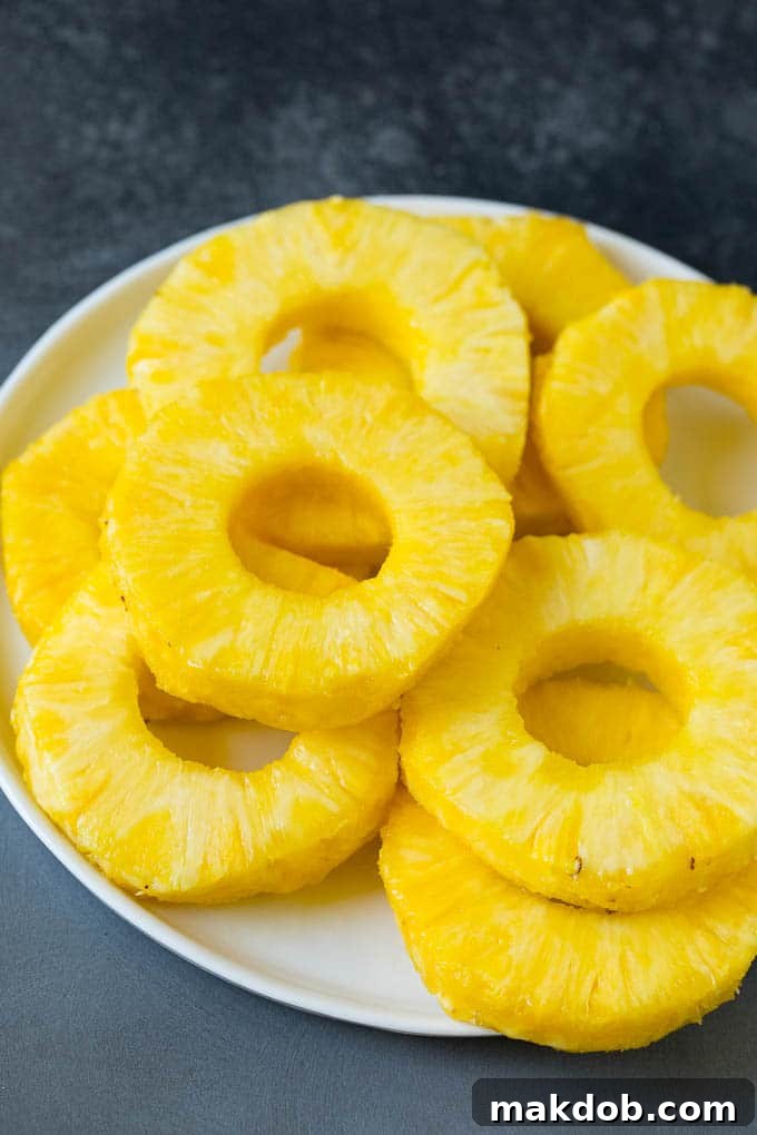 Slices of fresh pineapple and a bowl of butter, brown sugar, and cinnamon mixture on a plate, ready for grilling.
