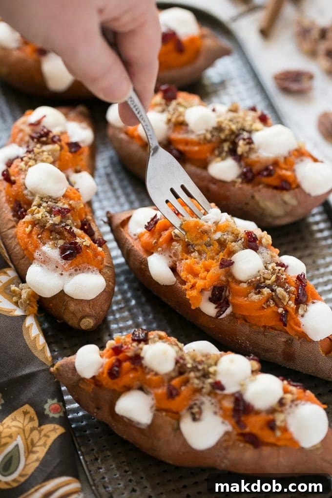 A fork gently lifting a serving of the creamy mashed filling, streusel, and melted marshmallows from a baked sweet potato, showcasing its tempting layers.