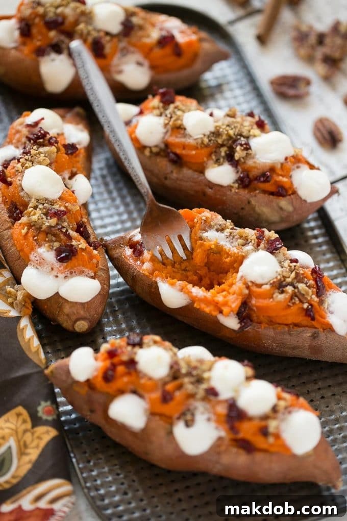 Several perfectly prepared twice baked sweet potatoes on a baking sheet, with one featuring a fork removing some of its delightful mashed potato filling and toppings, highlighting its layers.