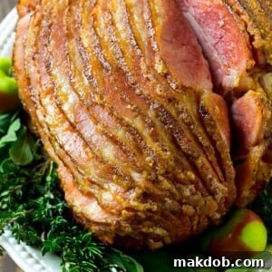 A magnificent spiral-cut honey-baked ham, beautifully arranged on a serving platter and garnished with fresh herbs.