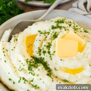 A bowl of luscious make-ahead mashed potatoes, generously topped with melted butter and fresh herbs.
