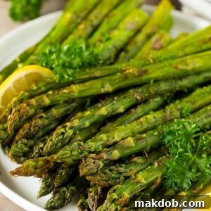 A plate of perfectly cooked air fryer asparagus, garnished with fresh lemon slices and a sprinkle of parsley.