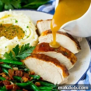 Rich, savory turkey gravy being poured gracefully over slices of tender turkey breast.