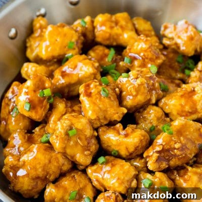 A pan of crispy honey chicken garnished with fresh green onions, showcasing its golden-brown texture and glossy sauce.