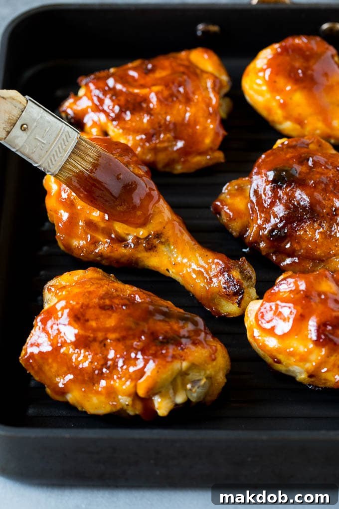 Super easy BBQ chicken that can be grilled or baked with perfect results every time! Barbecue sauce being brushed over grilled chicken.