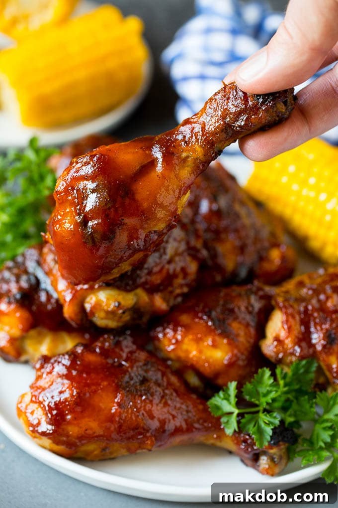 Super easy BBQ chicken that can be grilled or baked with perfect results every time! A hold holding a BBQ chicken drumstick.