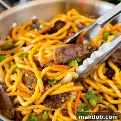 Tongs serving up a portion of beef lo mein.