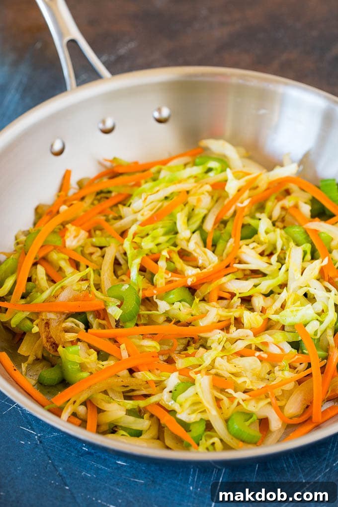 A vibrant mix of carrots, celery, and cabbage stir-frying in a hot pan, showing the beginning stages of creating a flavorful beef lo mein.