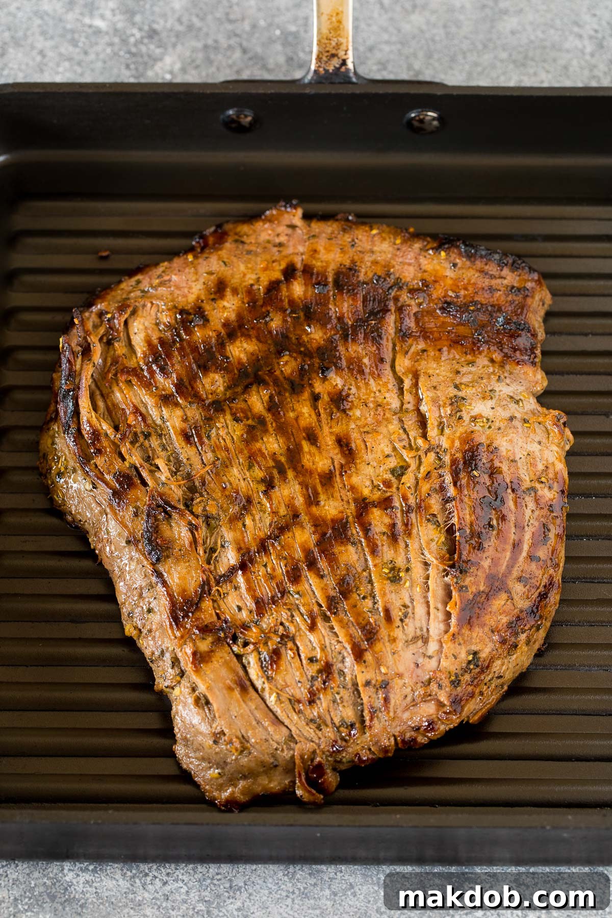Flank steak cooking on a ribbed grill pan, showing grill marks.