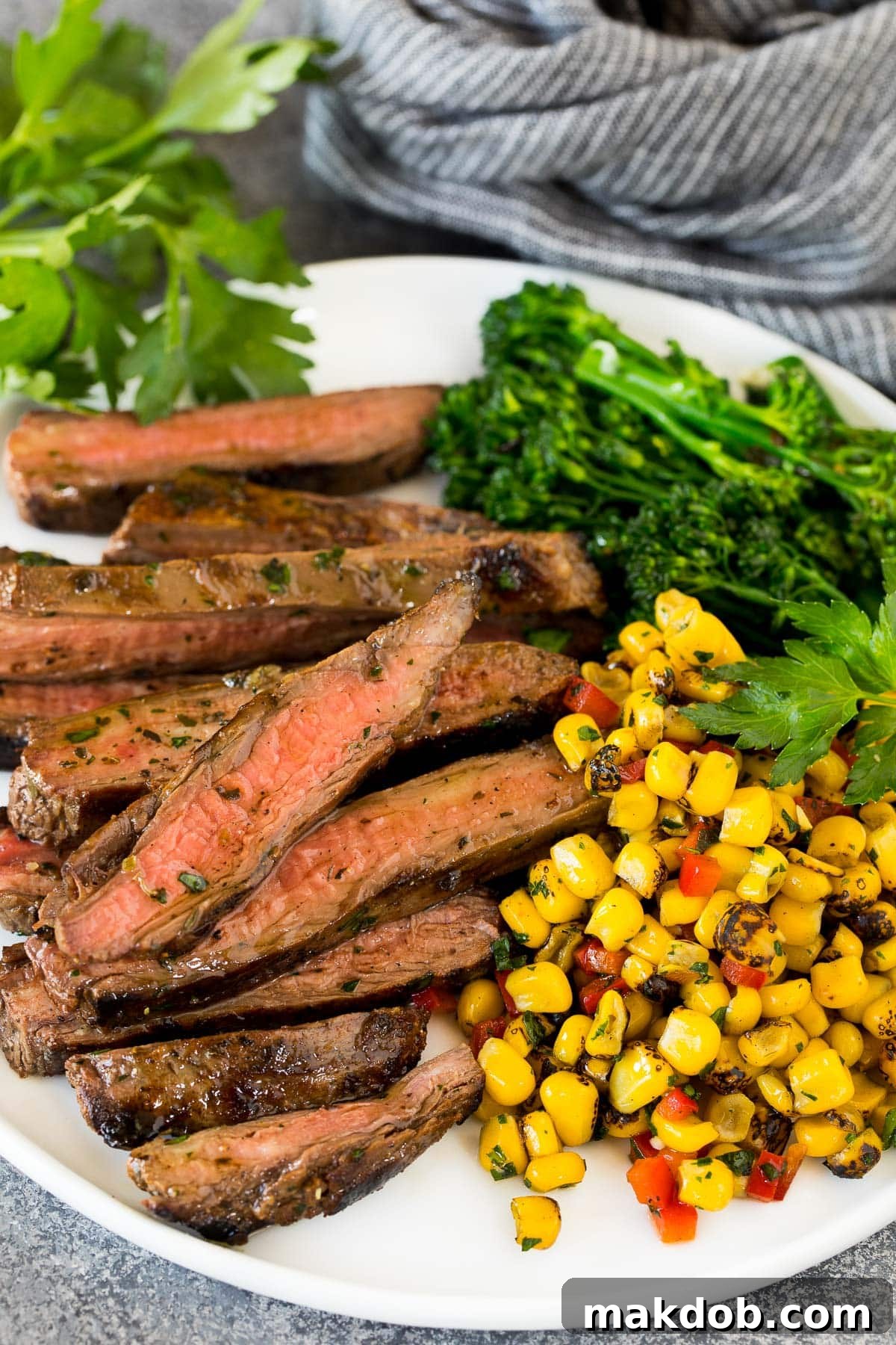 A serving of grilled flank steak with grilled corn on the cob and steamed broccoli.