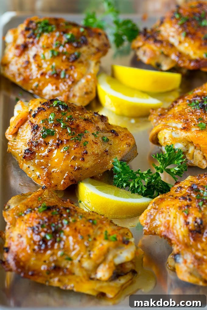 These baked chicken thighs are coated in olive oil, garlic and herbs, then oven roasted until golden brown. A pan of baked chicken thighs garnished with parsley and lemon.