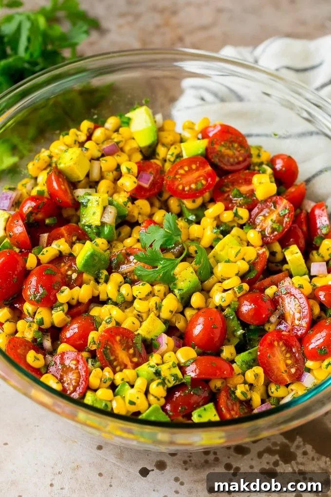A bowl of corn salad with avocado and tomato, all tossed in a lime dressing.