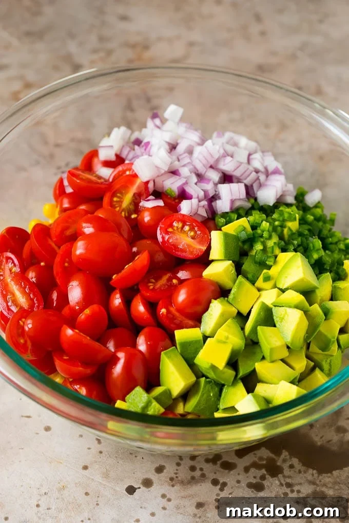 Corn, tomatoes, avocado, jalapeno and red onion in a bowl.