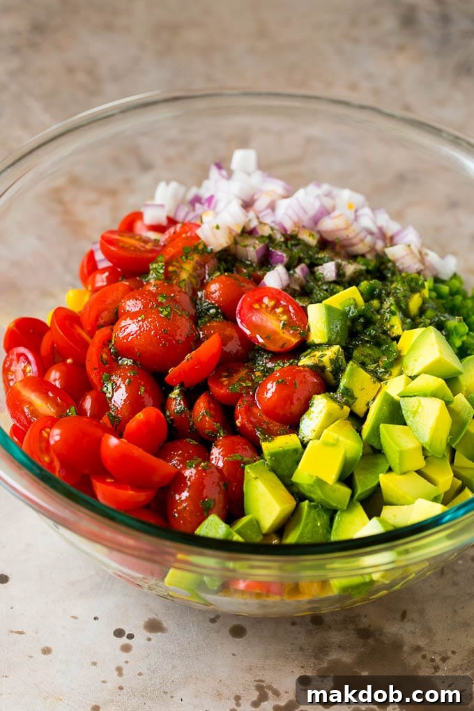 Dressing poured over tomatoes, corn and avocado in a salad bowl.