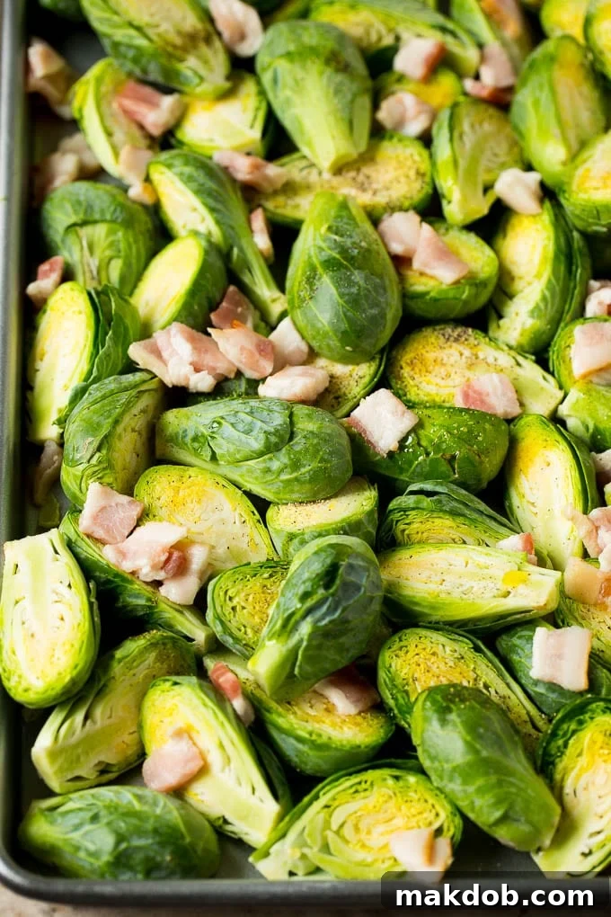 Brussels sprout halves and chopped bacon scattered on a sheet pan.