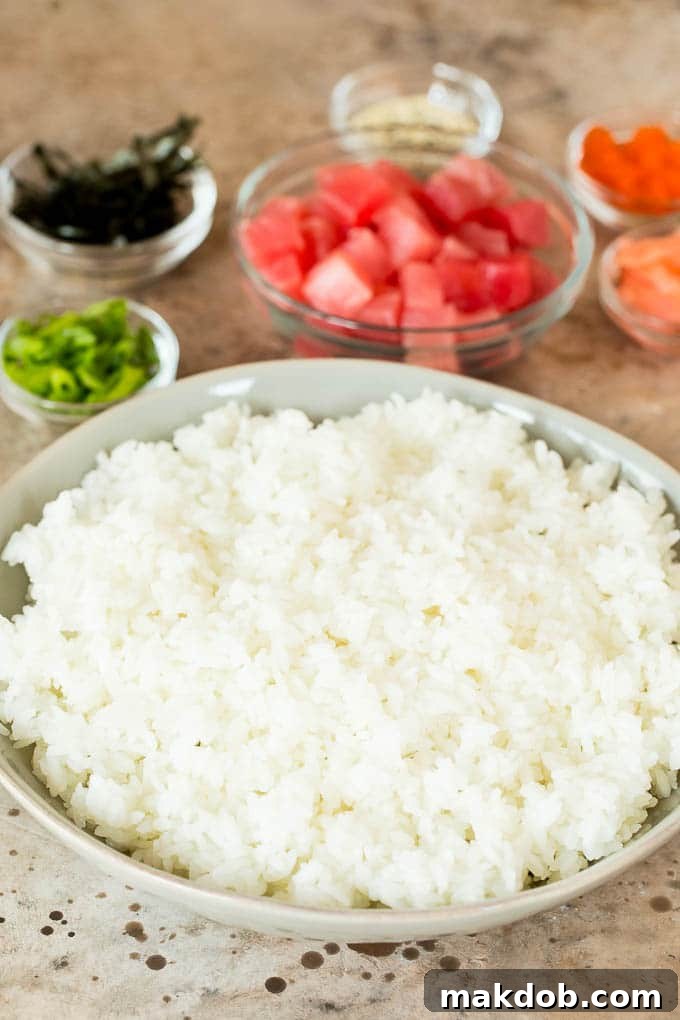 This sushi bowl recipe is assorted fresh fish, avocado, cucumber and seaweed, all served over rice with spicy mayo, picked ginger and tobiko. A bowl of sushi rice with bowls of toppings around it.
