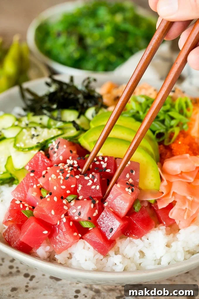 This sushi bowl recipe is assorted fresh fish, avocado, cucumber and seaweed, all served over rice with spicy mayo, picked ginger and tobiko. Chopsticks picking up a piece of ahi tuna in a sushi bowl.
