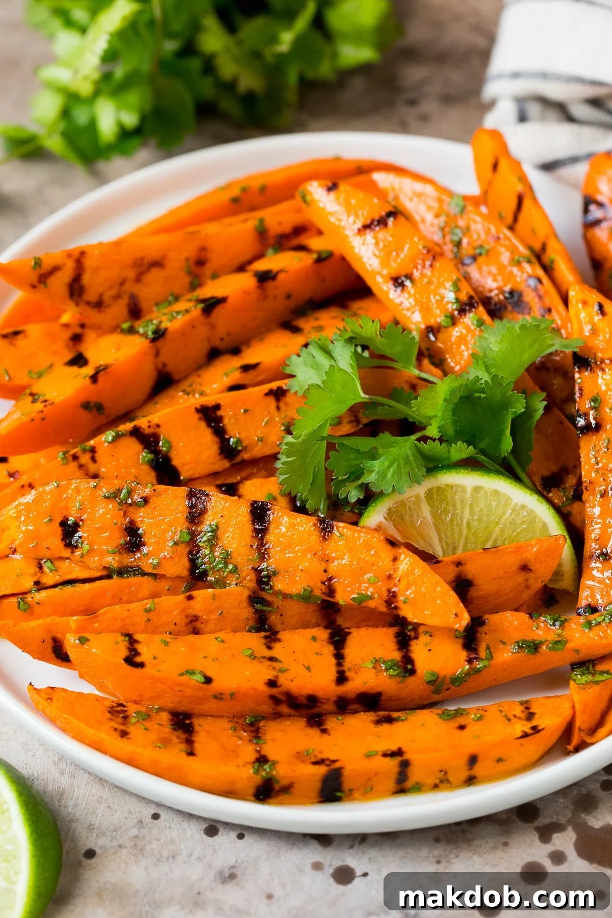 Fire-Kissed Sweet Potatoes 2 A plate of grilled sweet potatoes topped with cilantro lime dressing, garnished with fresh cilantro and lime wedges.