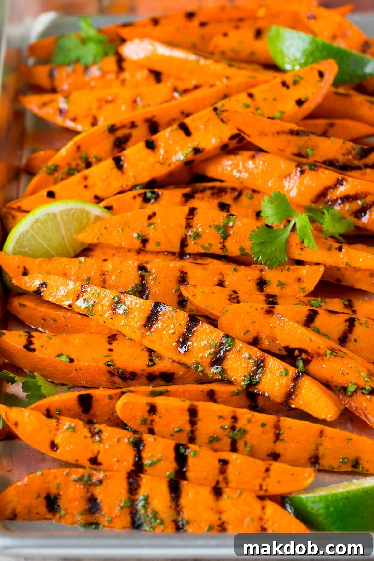 Fire-Kissed Sweet Potatoes 6 A sheet pan of grilled sweet potatoes garnished with fresh lime wedges and cilantro sprigs.