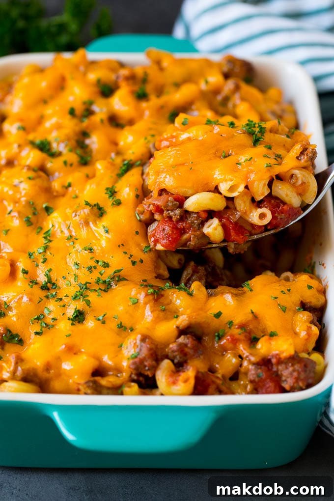 A comforting serving of hamburger casserole with pasta, ground beef, and melted cheddar cheese. A spoon serving up a portion of hamburger casserole made with pasta and melted cheese.