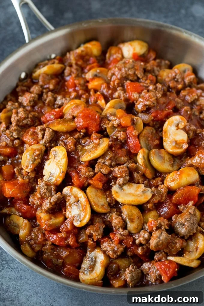 The hearty beef and tomato sauce mixture for the hamburger casserole. Ground beef, mushrooms, onions and diced tomatoes simmering together in a pan.