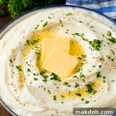 A bowl of cauliflower mashed potatoes topped with melted butter and parsley, ready to be served as a low-carb side dish.