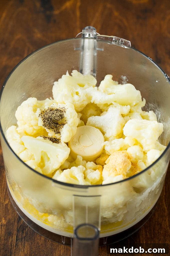 Pureeing Cauliflower for the Perfect Mash Cooked cauliflower, heavy cream, butter, and seasonings being added to a food processor for pureeing into mashed cauliflower.