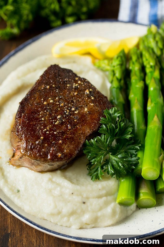 Serving Cauliflower Mashed Potatoes with Steak and Asparagus Cauliflower mashed potatoes served on a plate alongside a perfectly grilled steak and steamed asparagus, creating a balanced and healthy meal.