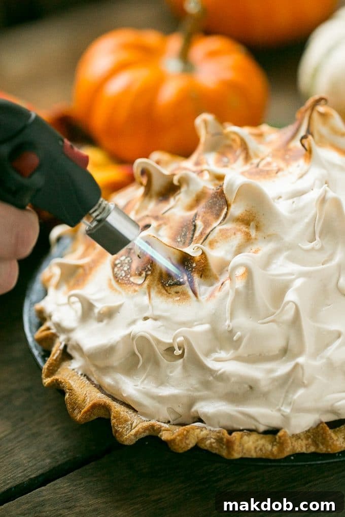 A focused shot of a kitchen torch delicately browning the peaks of meringue on a pumpkin pie, creating a beautiful caramelized crust.