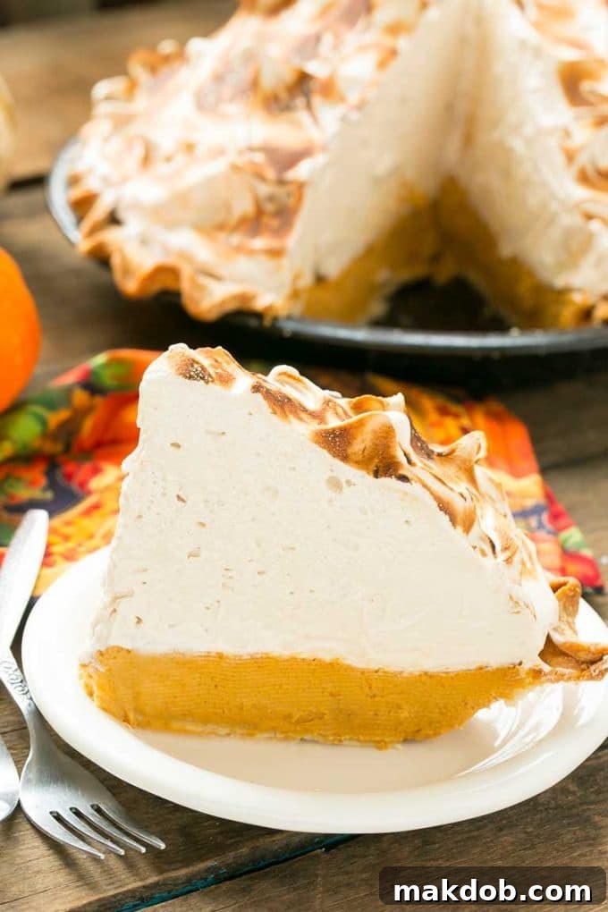 A perfectly cut slice of pumpkin meringue pie resting on a white plate, showcasing its creamy filling and fluffy toasted meringue.
