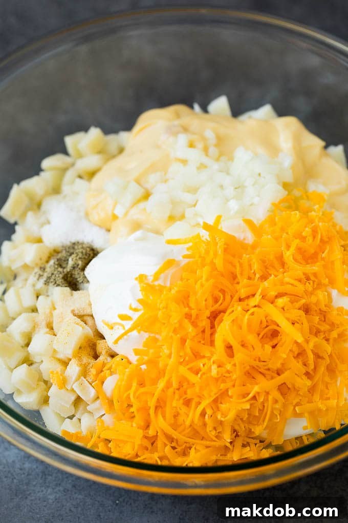 Mixing bowl with ingredients for the cheesy potato base of Funeral Potatoes. A large mixing bowl filled with thawed hash browns, sour cream, grated cheddar cheese, and various seasonings, ready to be combined.