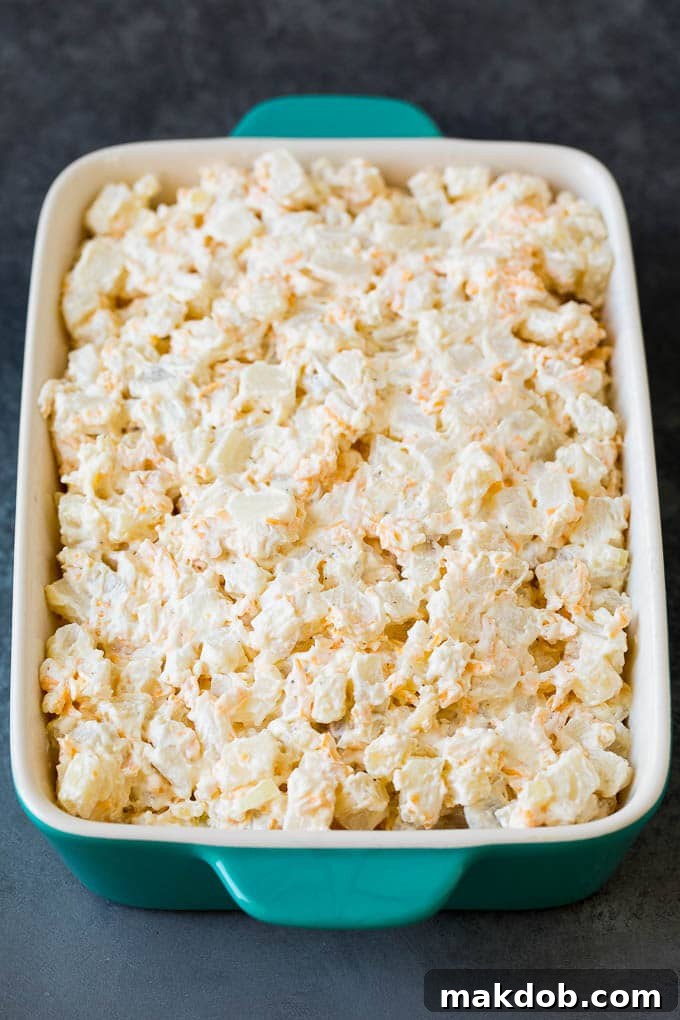 Unbaked Funeral Potato casserole in a dish, ready for topping. A close-up view of the uncooked funeral potato mixture in a glass baking dish, showing the creamy, cheesy potatoes before the cornflake topping is added.