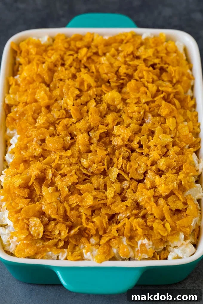 Baked Funeral Potatoes with a golden, crunchy cornflake topping. A golden-brown dish of cheesy funeral potatoes, topped with a perfectly crisp cornflake crust, garnished with fresh parsley.