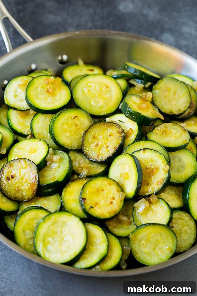Cooked slices of zucchini and diced onion in a skillet, ready for the next step.