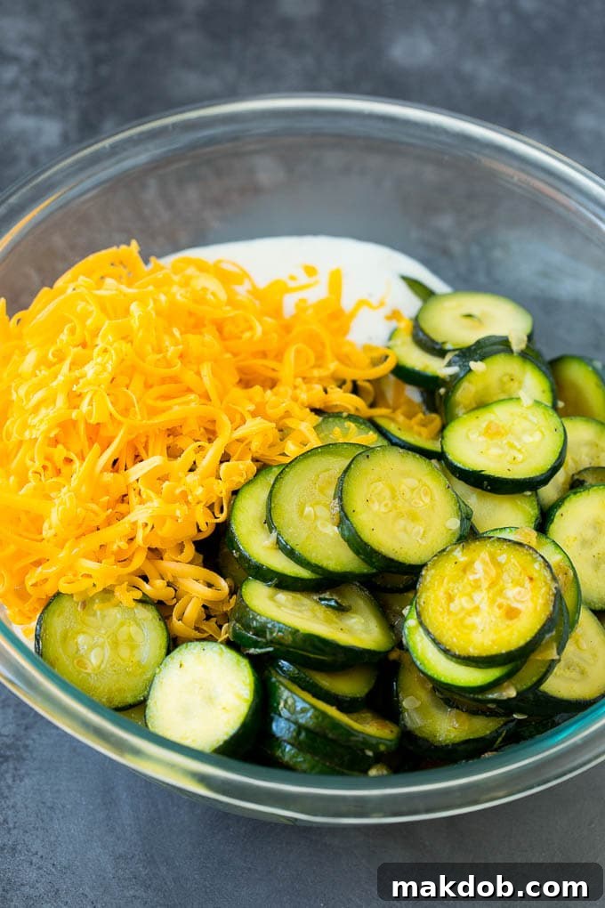 Zucchini, cheese, and creamy sauce mixed in a bowl, before being transferred to a baking dish.