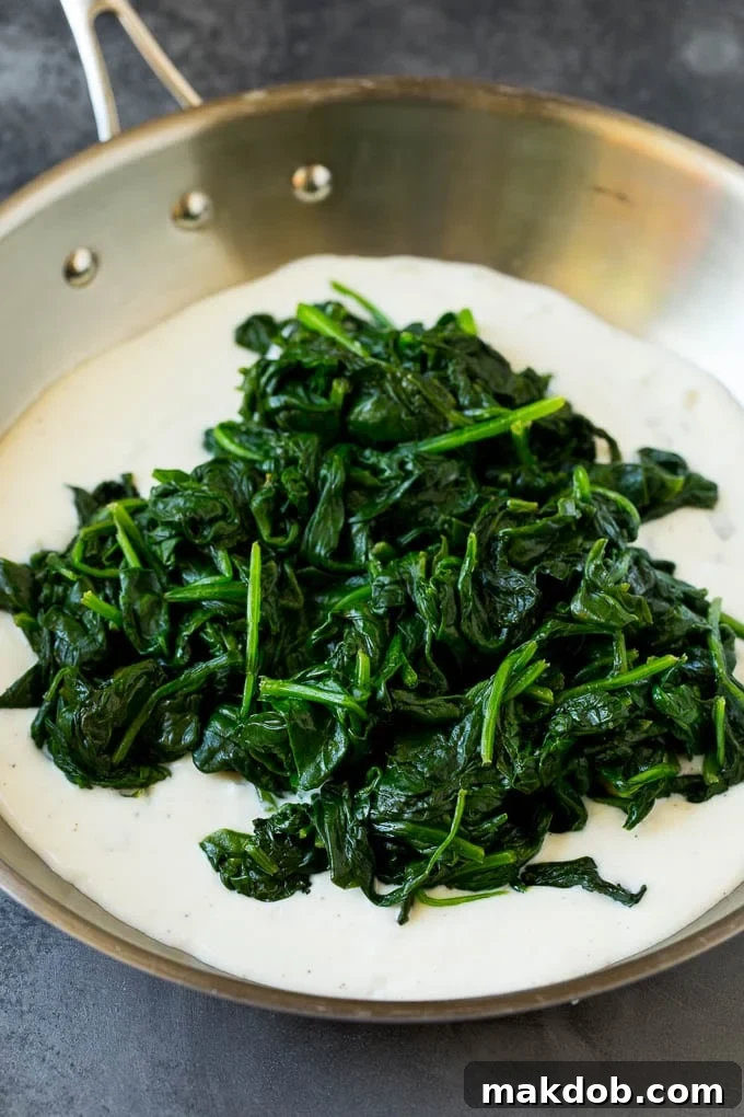 A rich cream sauce in a pan, with a generous pile of perfectly cooked spinach waiting to be stirred in.