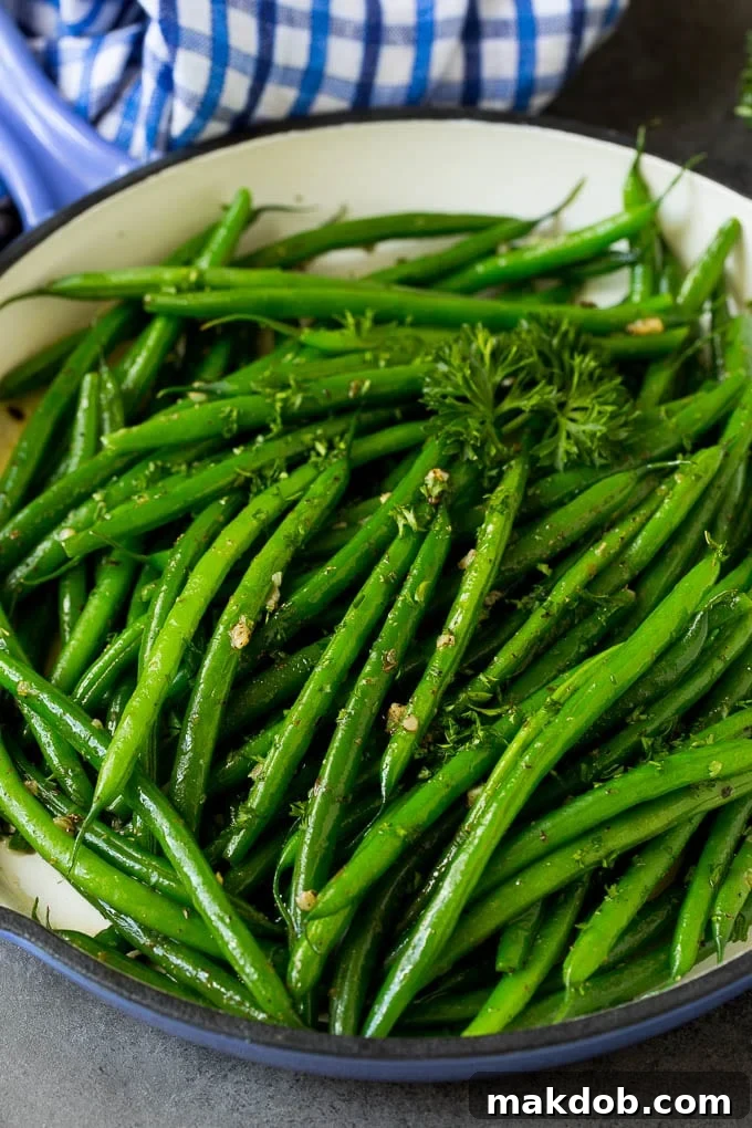 These sauteed green beans are cooked in butter, garlic and an assortment of fresh and dried herbs. A blue skillet filled with sauteed green beans, garnished with parsley.