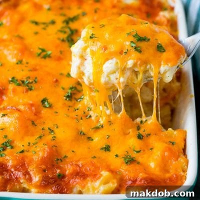 A spoon serving up a portion of cheesy potatoes topped with chopped parsley.
