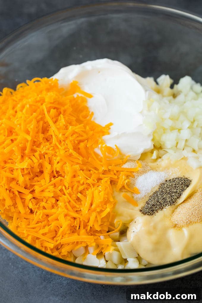 A large mixing bowl filled with diced potatoes, cream soup, generous shredded cheddar cheese, and various spices, ready to be combined.