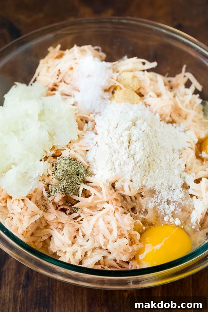 These potato pancakes are shredded potatoes combined with onions and seasoning, then pan fried until golden brown. Shredded potatoes, eggs and seasonings in a bowl.