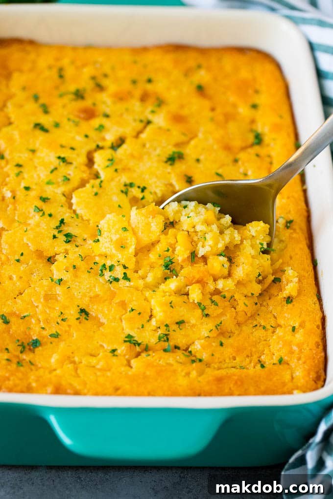 This corn souffle recipe is a flavorful blend of corn kernels, butter, eggs and creamed corn, all baked to light and fluffy perfection. A dish of corn souffle with a serving spoon in it, showcasing its light and fluffy texture.