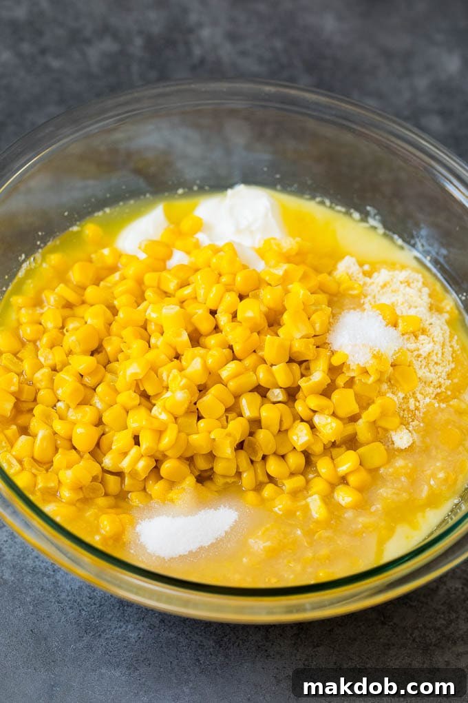 This corn souffle recipe is a flavorful blend of corn kernels, butter, eggs and creamed corn, all baked to light and fluffy perfection. Corn muffin mix, corn kernels, sour cream and seasonings in a bowl, ready to be mixed for corn souffle.