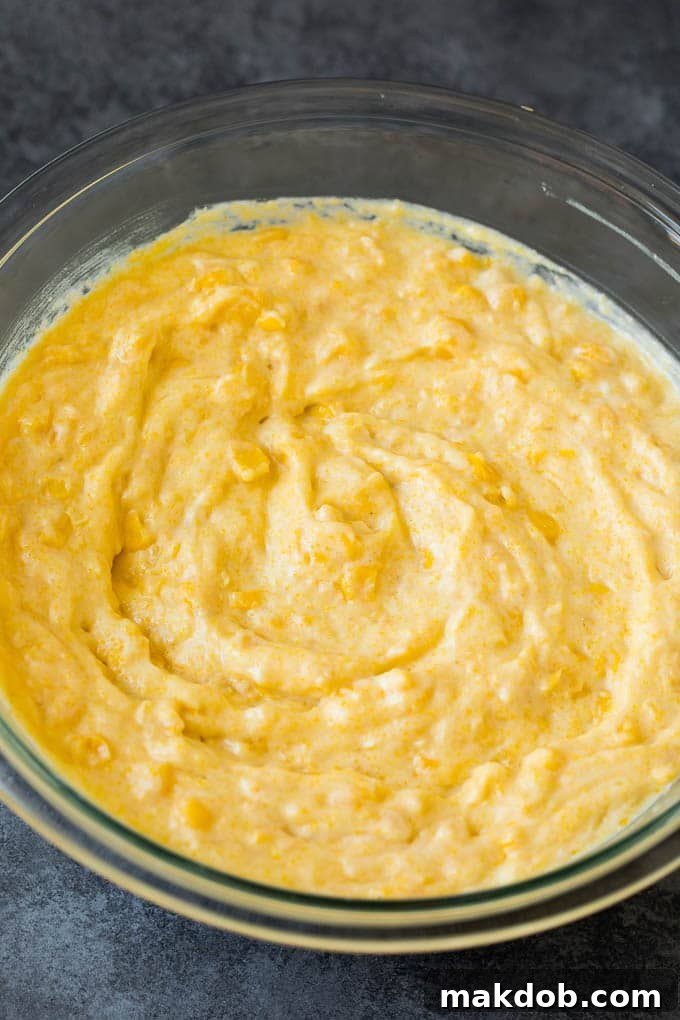This corn souffle recipe is a flavorful blend of corn kernels, butter, eggs and creamed corn, all baked to light and fluffy perfection. Batter in a mixing bowl, showing the creamy texture and corn kernels.